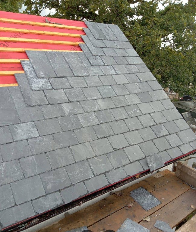 Grey slate tiles being laid over breathable membrane during a re-roof in Sandhurst