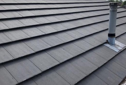 New grey tiled roof with tall vent pipe after a complete roof replacement