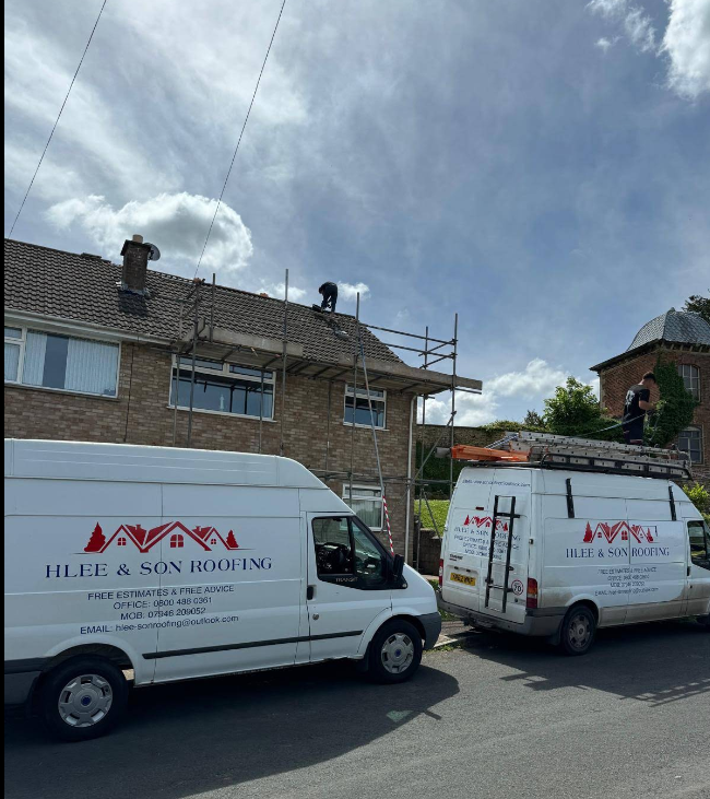 Two H Lee & Son Roofing vans parked outside a scaffolded house while the team works on the roof