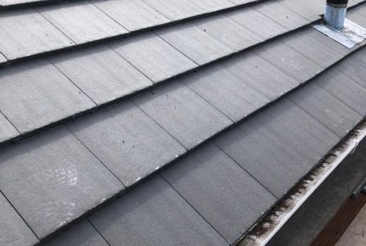 Close-up of uniform grey concrete roof tiles and a vent on a newly laid roof
