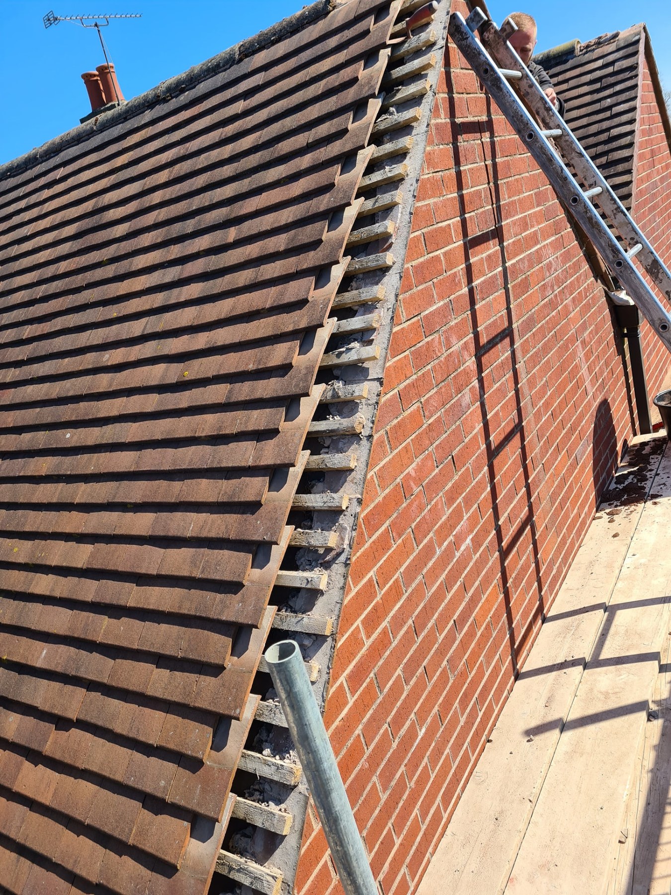 Roofer detailing tiles against a brick gable end during a roof replacement