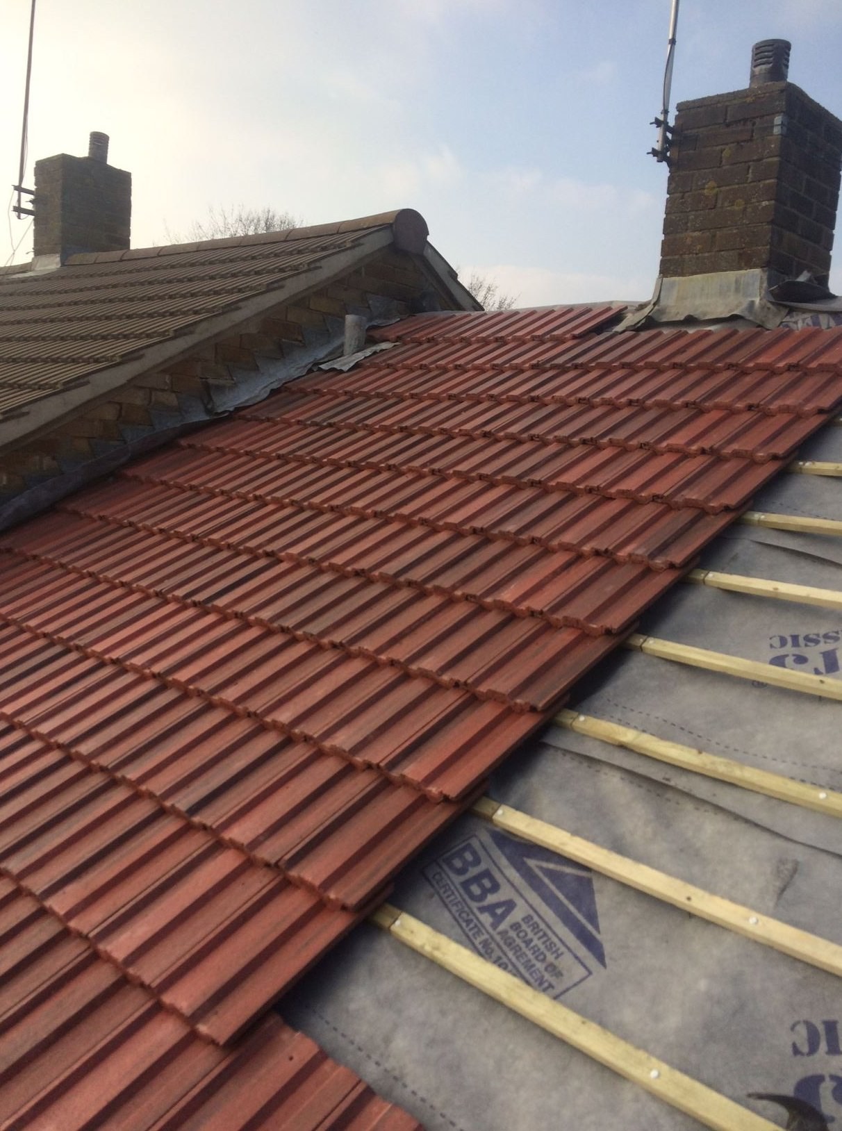 New red roof tiles being laid over breathable membrane and treated battens