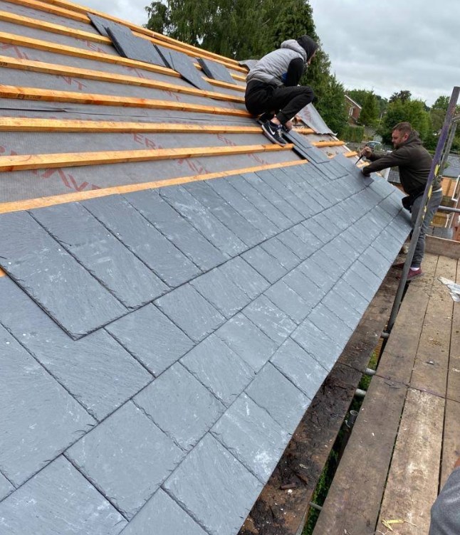 Roofer nailing grey slate tiles across a large roof slope